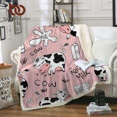 a pink blanket with black and white farm animals on it is sitting in front of a couch