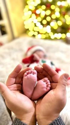 a person holding their baby's feet in front of a christmas tree with lights