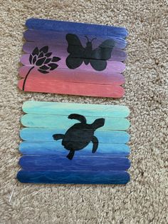 three different colored wooden sticks with black silhouettes of turtles and flowers on them, each painted in different colors