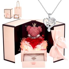 a teddy bear in a gift box with flowers and a heart shaped necklace on it