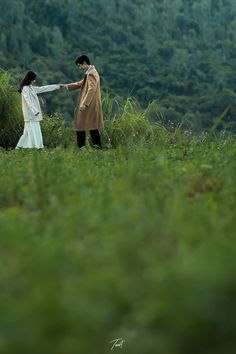 two people standing in the grass holding hands