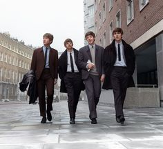 the beatles walking down a city street in front of tall buildings with one man wearing a suit and tie