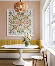 a white table sitting under a painting next to a yellow bench with flowers on it