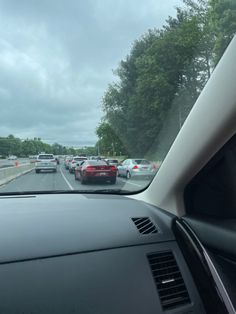 cars driving down the road in traffic on a cloudy day with trees and bushes behind them