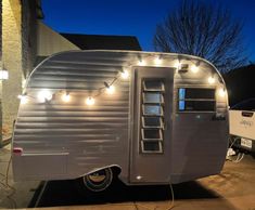 a silver trailer parked in front of a house with lights on it's side