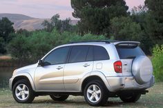 a silver suv parked next to a body of water with trees and bushes in the background