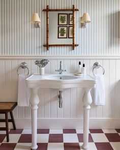 a white sink sitting under a bathroom mirror next to a wooden stool and wall mounted faucet