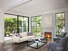 a living room filled with furniture next to large windows and a fire place in the corner