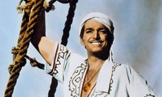 a man in white is holding on to a rope with one hand and smiling at the camera