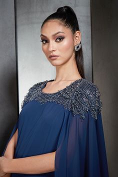 Galaxy blue long gown with cape sleeves and light beaded embroidery across the shoulders.
Component: 1
Pattern: Embroidered
Type Of Work: Bead Work
Neckline: Round
Sleeve Type: Cape Sleeves
Fabric: Georgette
Color: Blue
Other Details: 
Asymmetric cape sleeves
Back cut-out
Closure: Back zipper
Occasion: Cocktail - Aza Fashions Cape-shape Embellished Dress For Reception, Embellished Cape Dress For Reception, Embellished Gown With Cape Sleeves, Embellished Evening Dress With Cape Sleeves For Gala, Gala Embellished Evening Dress With Cape Sleeves, Elegant Blue Evening Dress With Cape Sleeves, Embellished Evening Dress With Cape Sleeves For Reception, Embellished Gown With Cape Sleeves For Gala, Elegant Blue Gown With Cape Sleeves