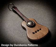 a wooden guitar keychain sitting on top of a gray surface with the words design by outdoorss patterns