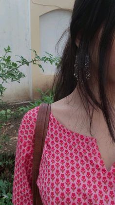 a woman with long black hair wearing a pink shirt and carrying a brown purse in her hand