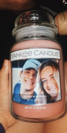 a person holding up a yankee candle with a picture on the front and back of it