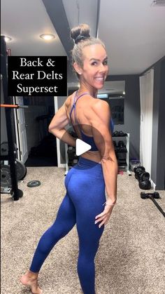 a woman standing in a gym room with her back to the camera and showing off her muscles