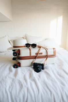 two suitcases with hats and sunglasses on top of a white bed in a room