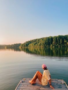 a woman sitting on the end of a dock looking out over a body of water