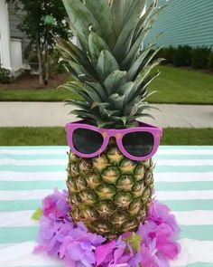 a pineapple wearing pink sunglasses on top of a blue and white striped table cloth