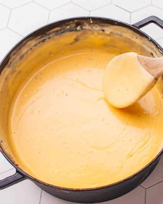 a wooden spoon in a large pot filled with yellow sauce on a white tile floor