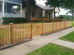 a wooden fence in front of a house with grass and trees on the side walk