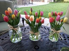 four vases filled with colorful tulips on top of a table in front of a patio