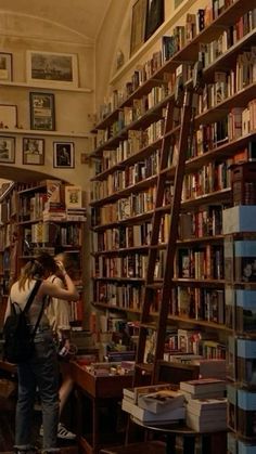 two people standing in front of a bookshelf with many books on the shelves