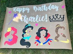 a birthday card with princesses on it sitting in the grass next to a sign that says happy birthday charlie