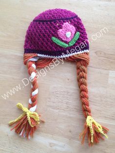 a crocheted hat with braids and flowers on the side, sitting on a wooden surface