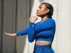 a woman with dreadlocks standing in front of a building wearing a blue top