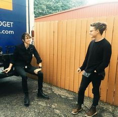 two young men are sitting on the back of a truck and talking to each other