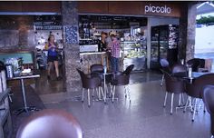 there are many chairs and tables in this restaurant with people standing outside the store front