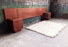 a wooden bed with a white rug on the floor in front of an old wall