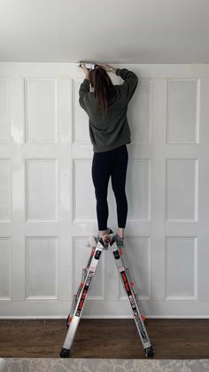 a woman standing on top of a steplade while holding onto the side of a wall