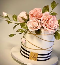 a white cake with pink roses on top and black stripes around the bottom, sitting on a table