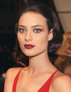 a woman in a red dress with dark lipstick on her face and hands behind her head