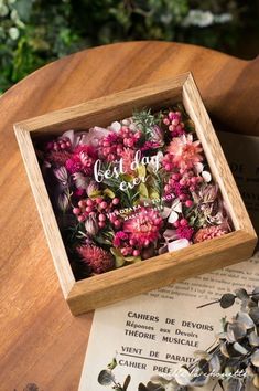 a wooden box filled with pink flowers on top of a table next to an open book