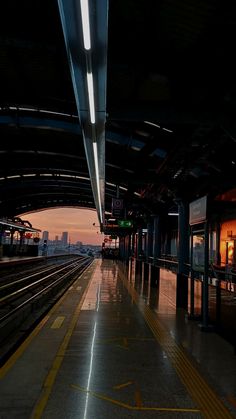 an empty train station at night with the sun setting on the horizon and buildings in the background