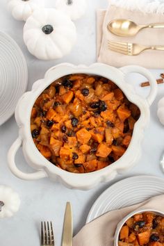 a white bowl filled with food next to plates and silverware on top of a table