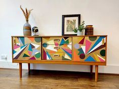 an artisticly painted dresser in the corner of a room with wood flooring and white walls