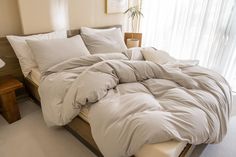 an unmade bed with white sheets and pillows in a bedroom next to a window