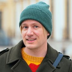 a man wearing a green hat and coat with a red stripe on the chest is smiling