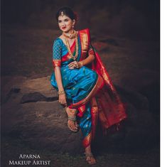 a woman sitting on top of a rock wearing a blue and red sari dress