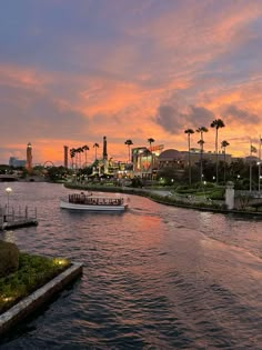 a boat traveling down a river next to palm trees and buildings in the background at sunset