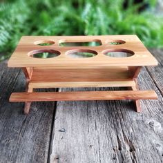 a small wooden tray with holes in it on a table next to some green plants