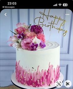 a white cake with pink and purple flowers on it's top is decorated with the words happy birthday