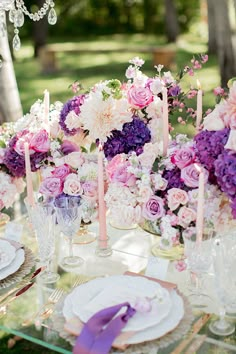 a table topped with lots of purple and white flowers next to tall vases filled with candles