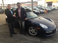 two men standing next to a black sports car