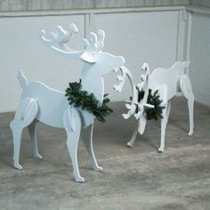 two white reindeer statues with christmas wreaths on their antlers