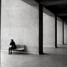 a woman sitting on a bench in an empty building with columns and concrete flooring