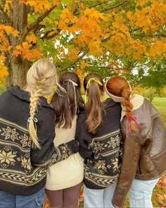 three girls standing in front of a tree with autumn leaves on the ground and one girl has her back to the camera