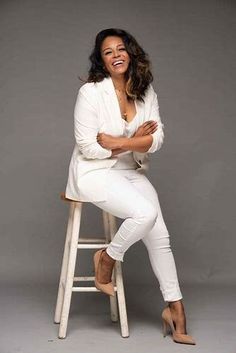 a woman sitting on top of a stool with her arms crossed and legs crossed, smiling